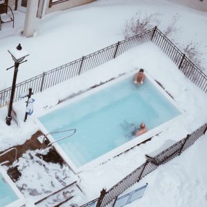 Two people sitting in a rectangular pool surrounded by snow
