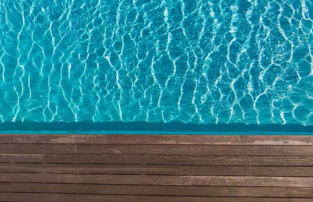 A closeup of a wooden poolside and blue water in the sun