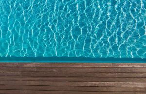 A closeup of a wooden poolside and blue water in the sun