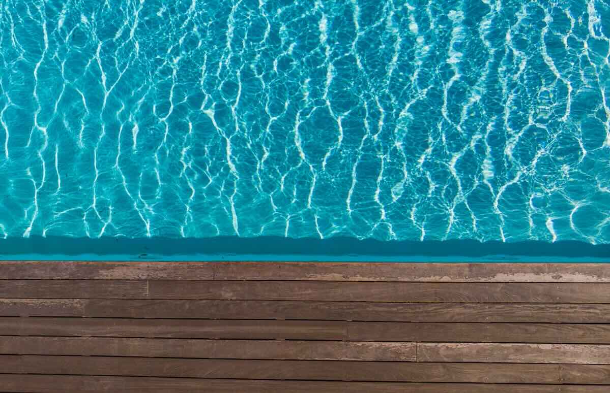 A closeup of a wooden poolside and blue water in the sun