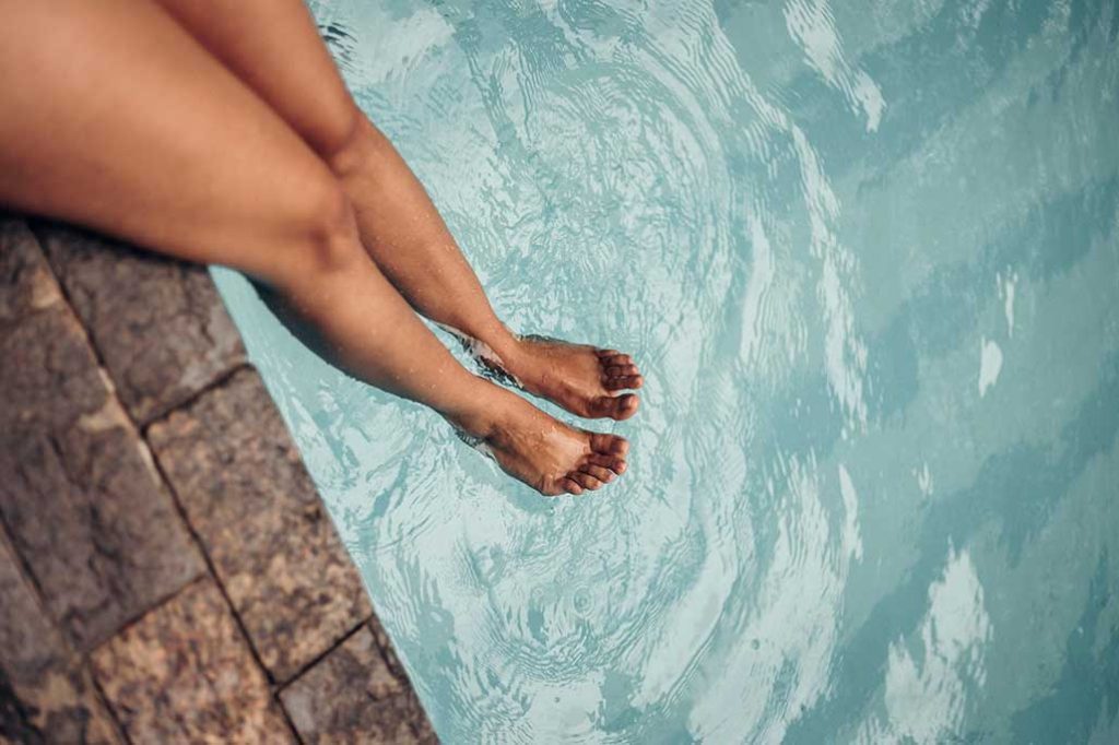 legs of woman dipping heels in pool