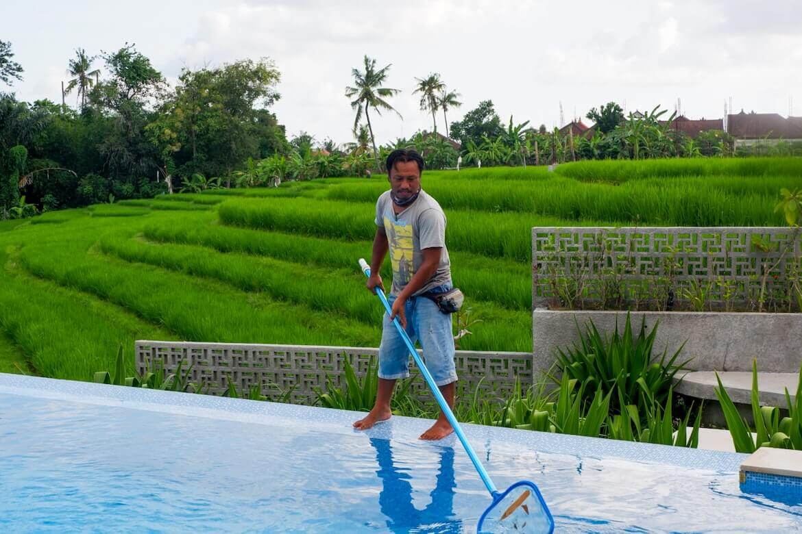 A man cleaning his inground pool with a skimming net
