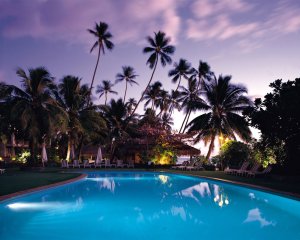 A blue, well lit pool, in the sunset of a tropical setting