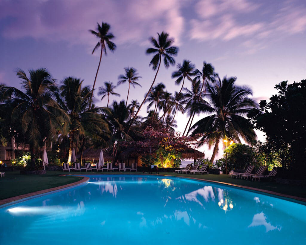 A blue, well lit pool, in the sunset of a tropical setting